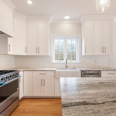 Bright white kitchen with stainless stove, farmhouse sink, and gray-veined island countertop