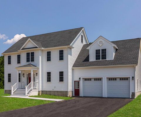 White two-story suburban house with attached two-car garage and dark gray roof under a blue sky