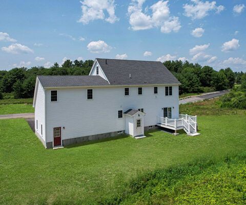 White church building with a small entry porch on a grassy hill under a blue sky with clouds