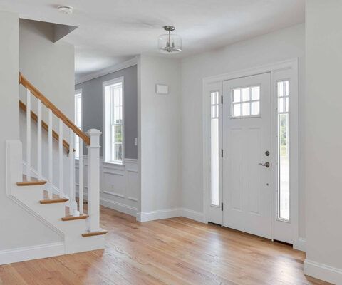 Bright entryway with white walls, hardwood floors, staircase, and a front door with sidelights.