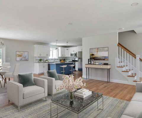 Bright open-plan living room with white armchair, glass coffee table, kitchen, and staircase
