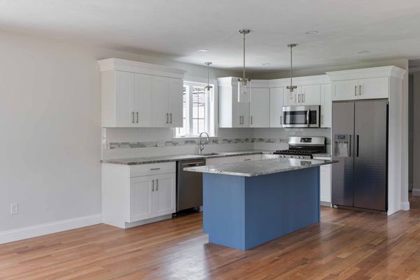 Modern kitchen with white cabinets, stainless steel appliances, and a blue island on hardwood floors