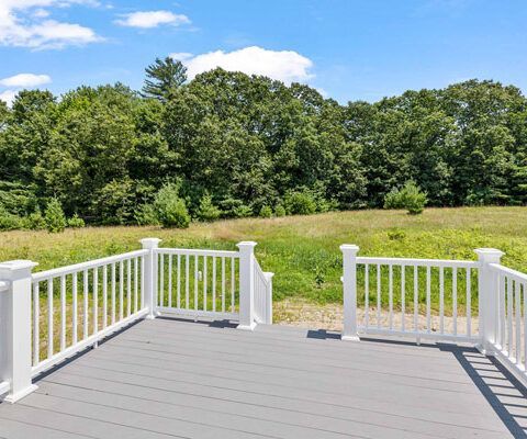 White-railed deck overlooking a grassy field and trees under a bright blue sky