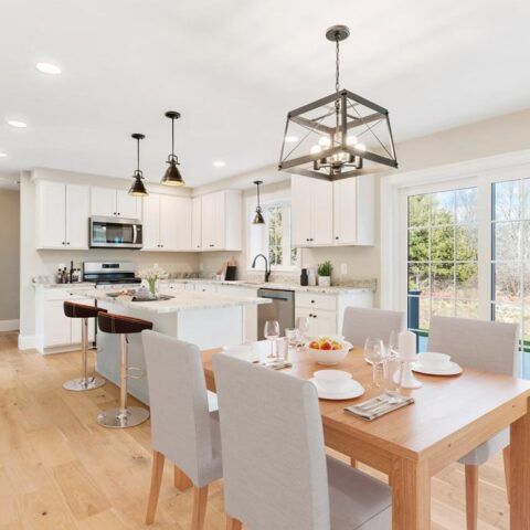 Bright modern kitchen and dining area with white cabinets, wood table, and pendant lights