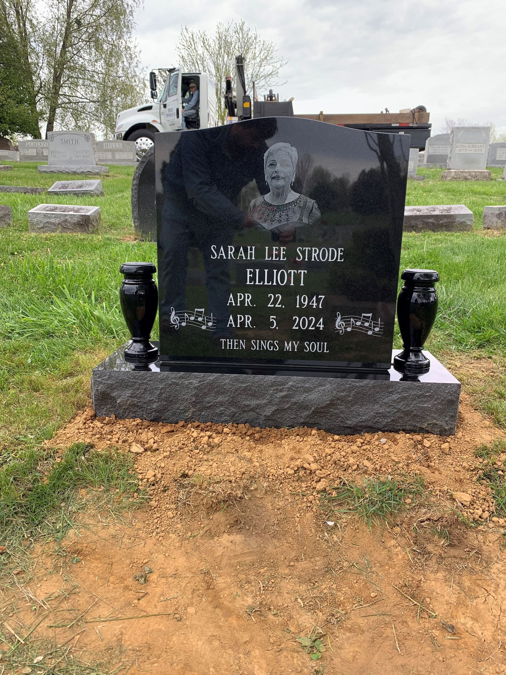 A gravestone in a cemetery with a truck in the background.