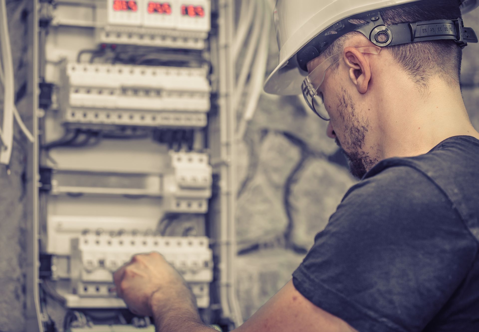 Un homme portant un casque et des lunettes de sécurité travaille sur un boîtier électrique.