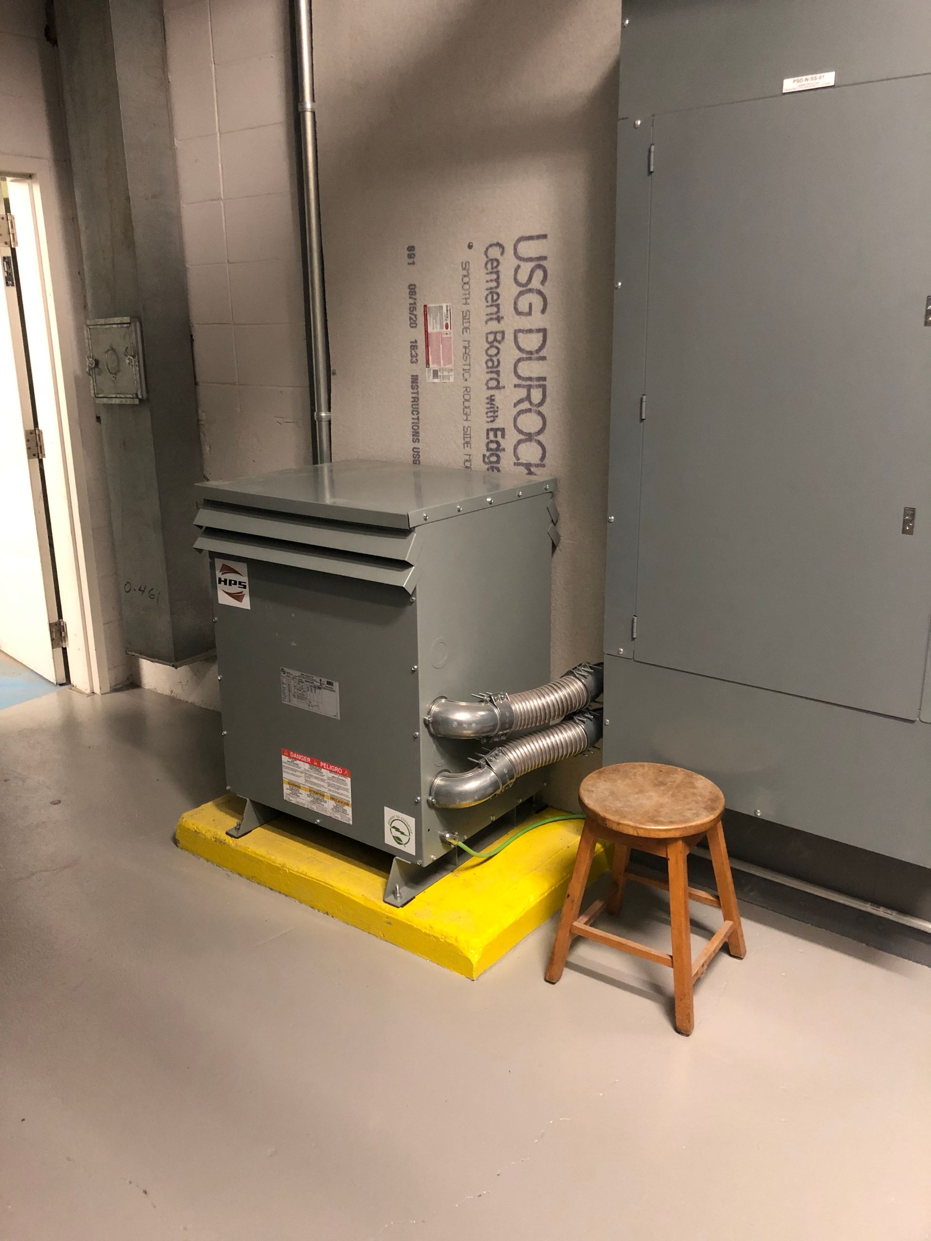 Un tabouret en bois est posé à côté d'un transformateur dans une pièce.