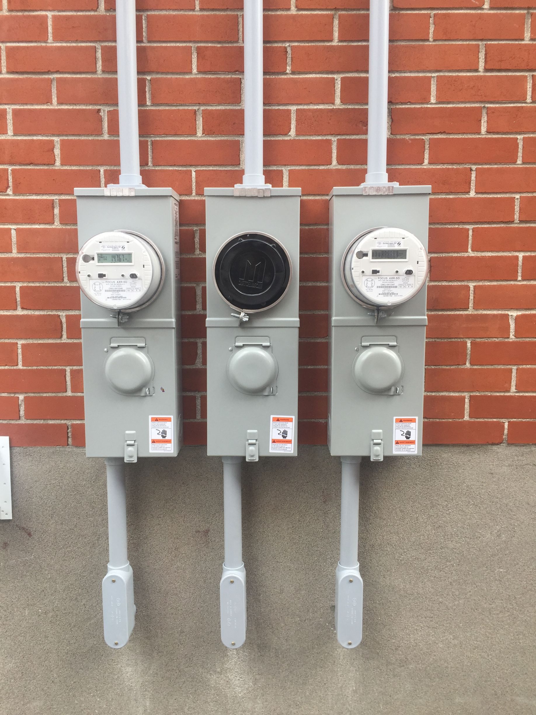 Trois boîtiers électriques sont alignés sur un mur de briques.