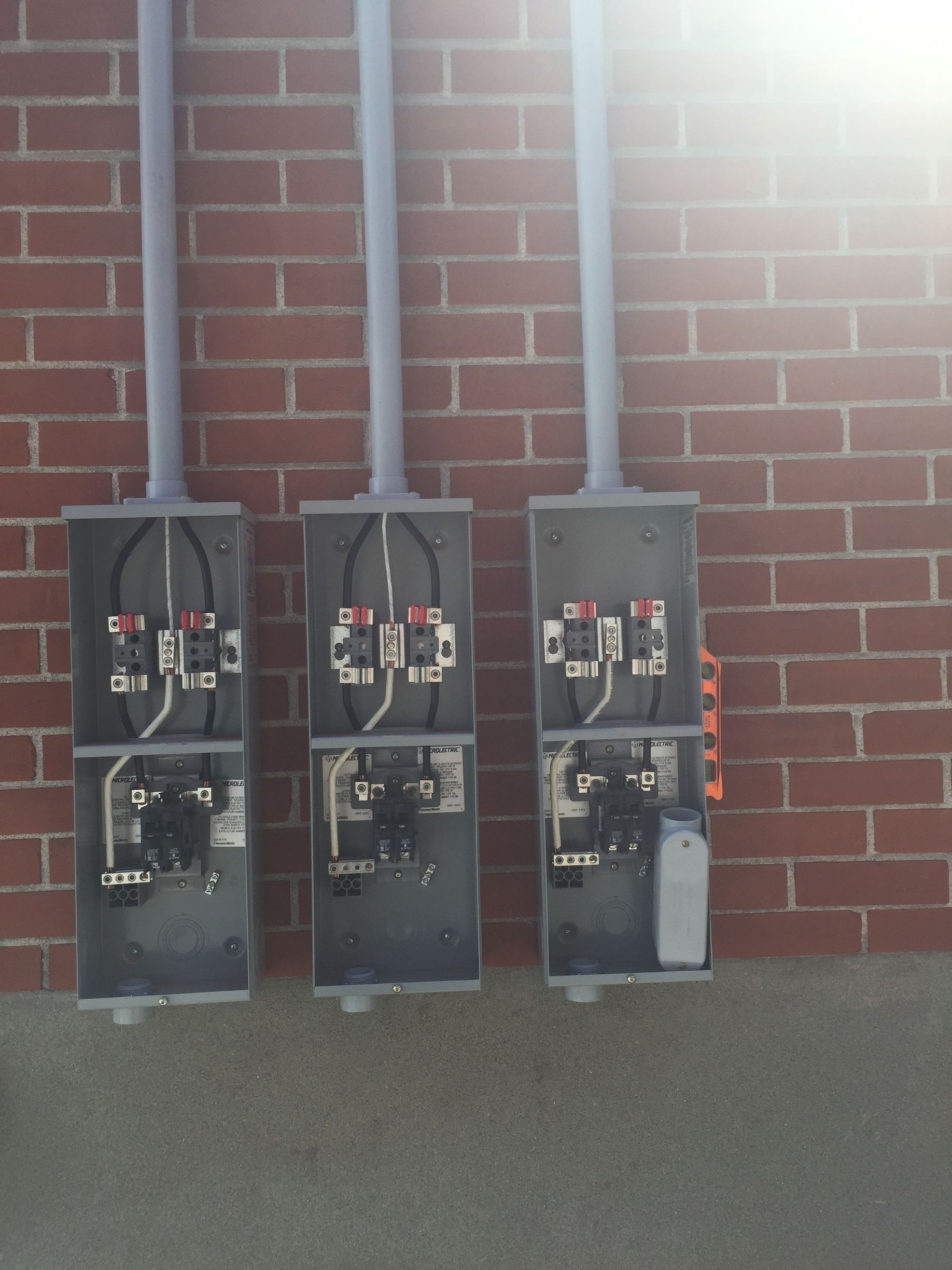 Trois boîtiers électriques sont alignés contre un mur de briques