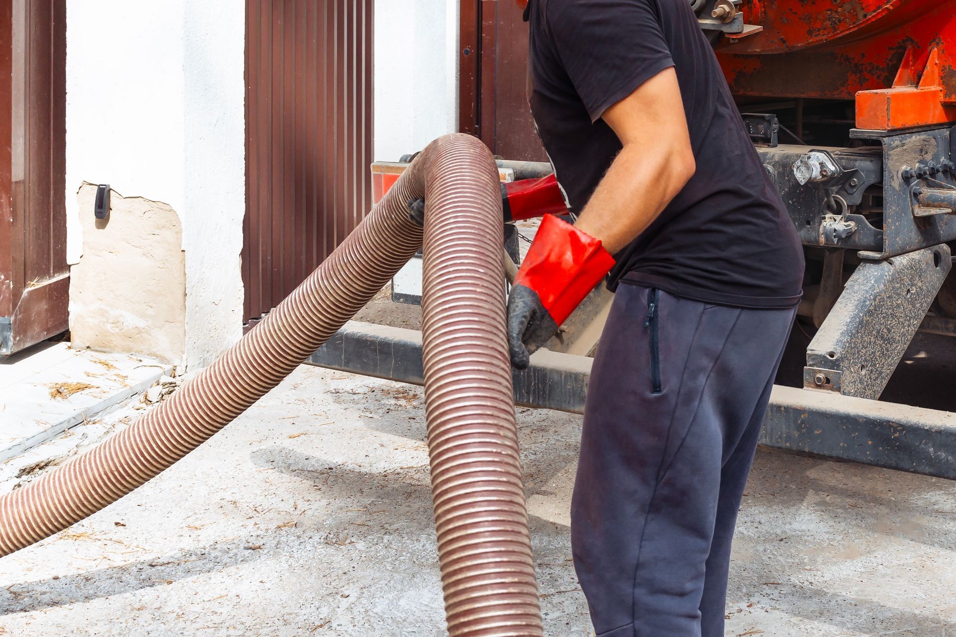 Man in red gloves holding a large hose near a truck; possibly related to sewage or waste management.