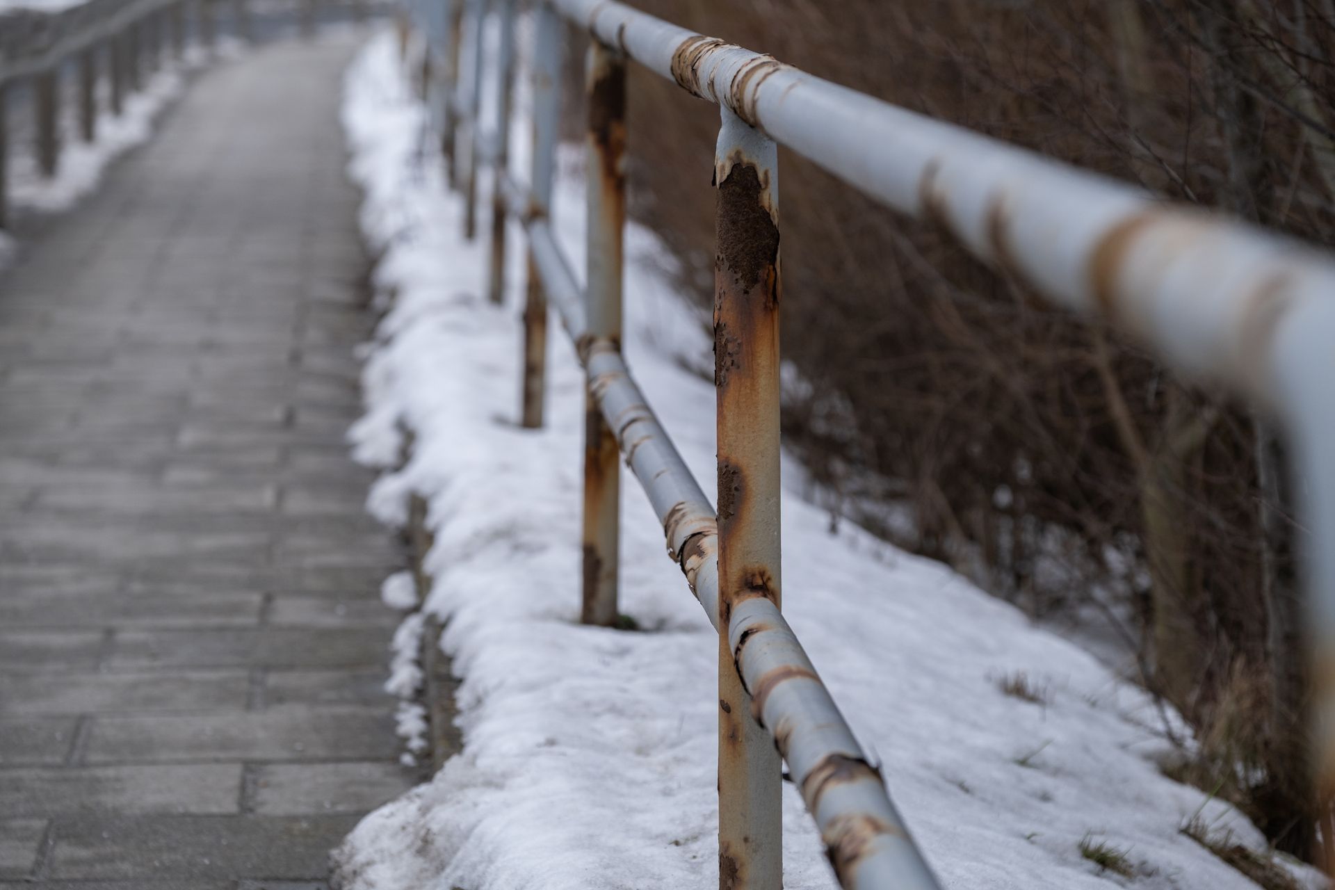 Rambarde rouillée le long d'un trottoir enneigé, sur un chemin étroit.
