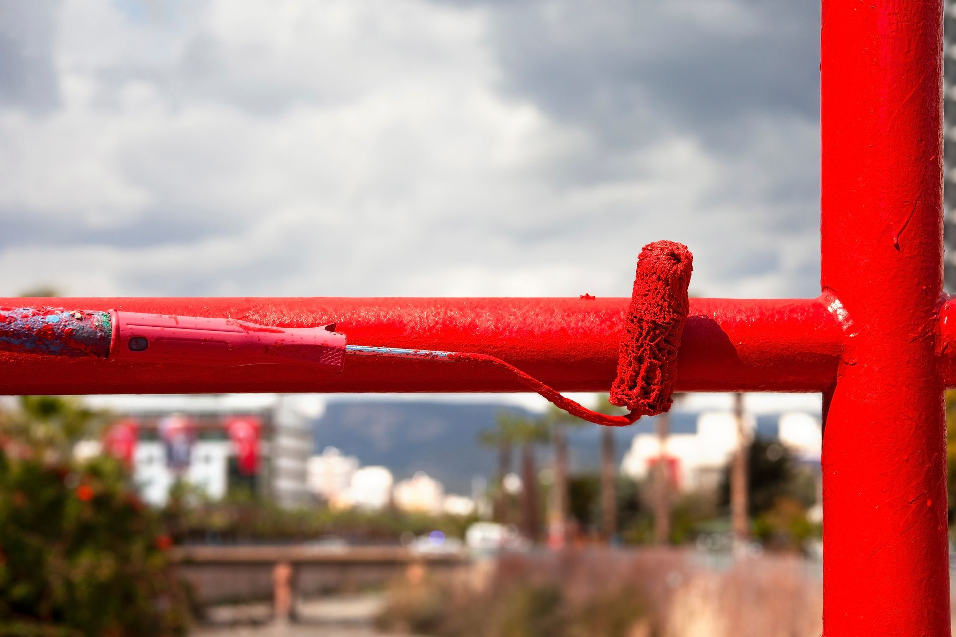 Rail métallique rouge au premier plan, ciel nuageux et paysage urbain flou en arrière-plan.