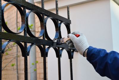 Main gantée appliquant de la peinture en aérosol sur une clôture métallique noire percée d'ouvertures circulaires