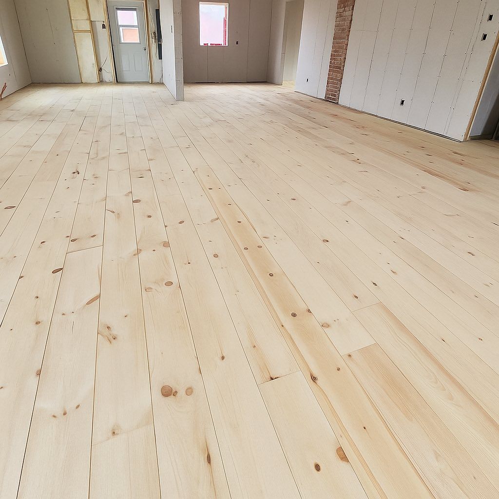 Pièce vide et inachevée, avec un parquet clair et des murs blancs, donnant sur les portes et les fenêtres.