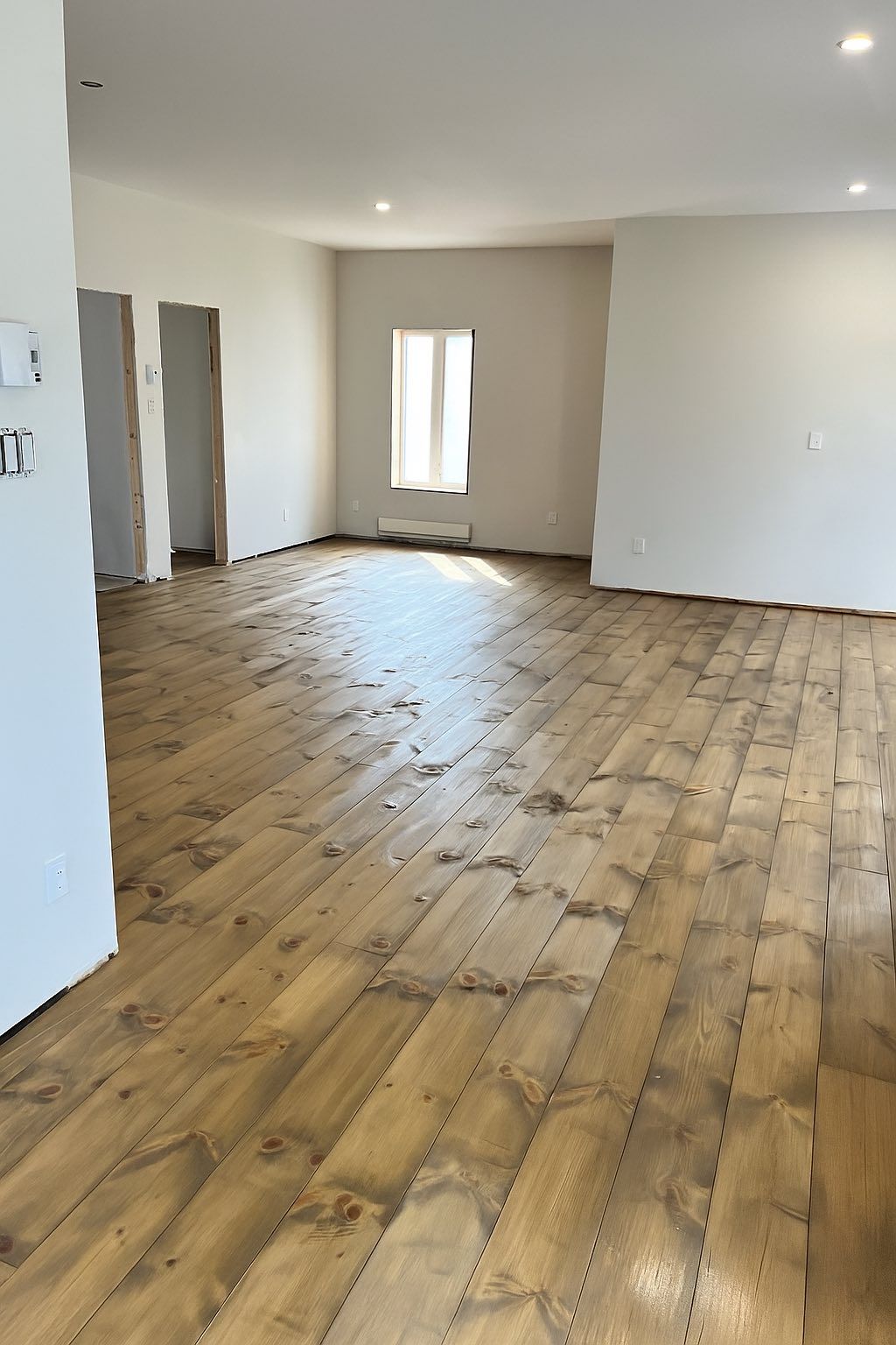 Pièce vide avec parquet clair, murs blancs et petite fenêtre