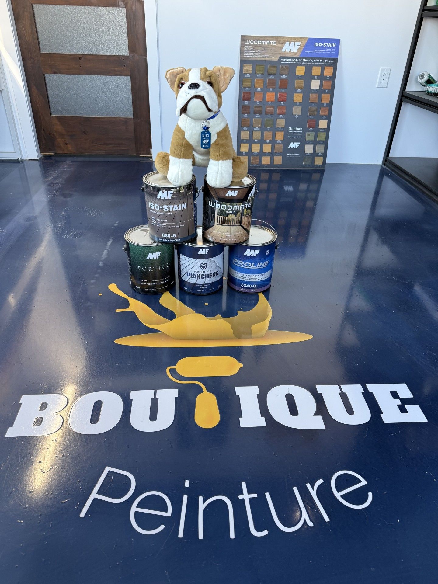 Présentoir de magasin de peinture avec une mascotte de bouledogue sur des pots de peinture et un nuancier, au-dessus du logo au sol « BOU TIQUE Peinture ».