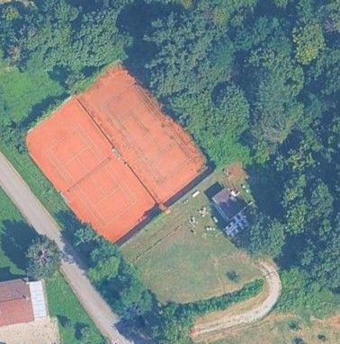 Vista dall'alto di due campi da tennis in terra battuta accanto a un edificio e circondati da alberi.