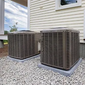 Two outdoor air conditioning units beside a house on a gravel bed