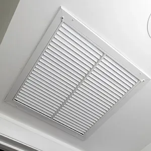 White ceiling vent with slatted grille in a light gray frame near the corner of a room