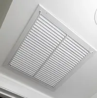 White ceiling vent with slatted grille in a light gray frame near the corner of a room