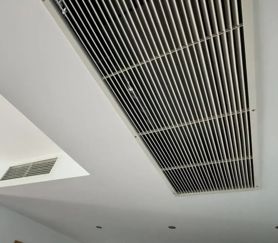 Ceiling with long black ventilation grille and recessed lights in a white room