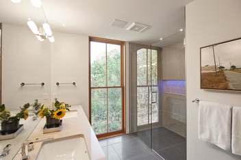 Modern bathroom with double vanity, glass shower, and large window beside a tiled floor.