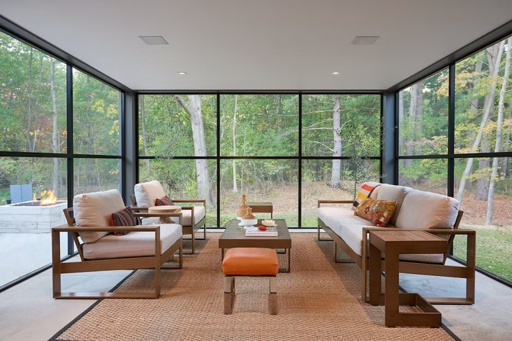 Modern living room with large glass windows, wooden sofas, and a central coffee table overlooking greenery