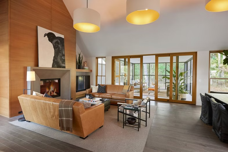 Modern living room with tan sofa, fireplace, glass doors, and warm pendant lights