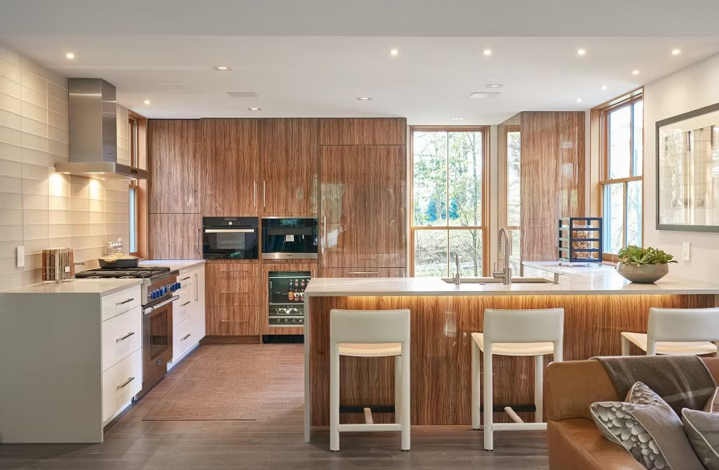 Bright modern kitchen with wood cabinets, white island, bar stools, and large windows