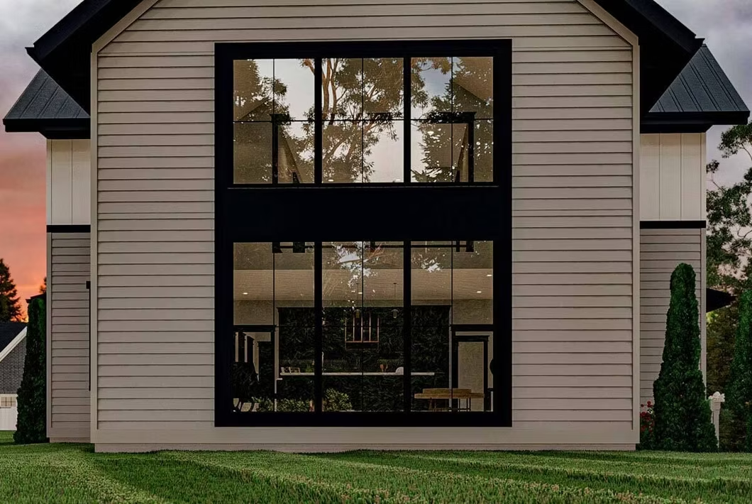 Modern two-story beige house with large black-framed windows at dusk