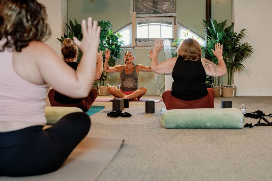 People seated in a yoga class raising their hands in a bright studio