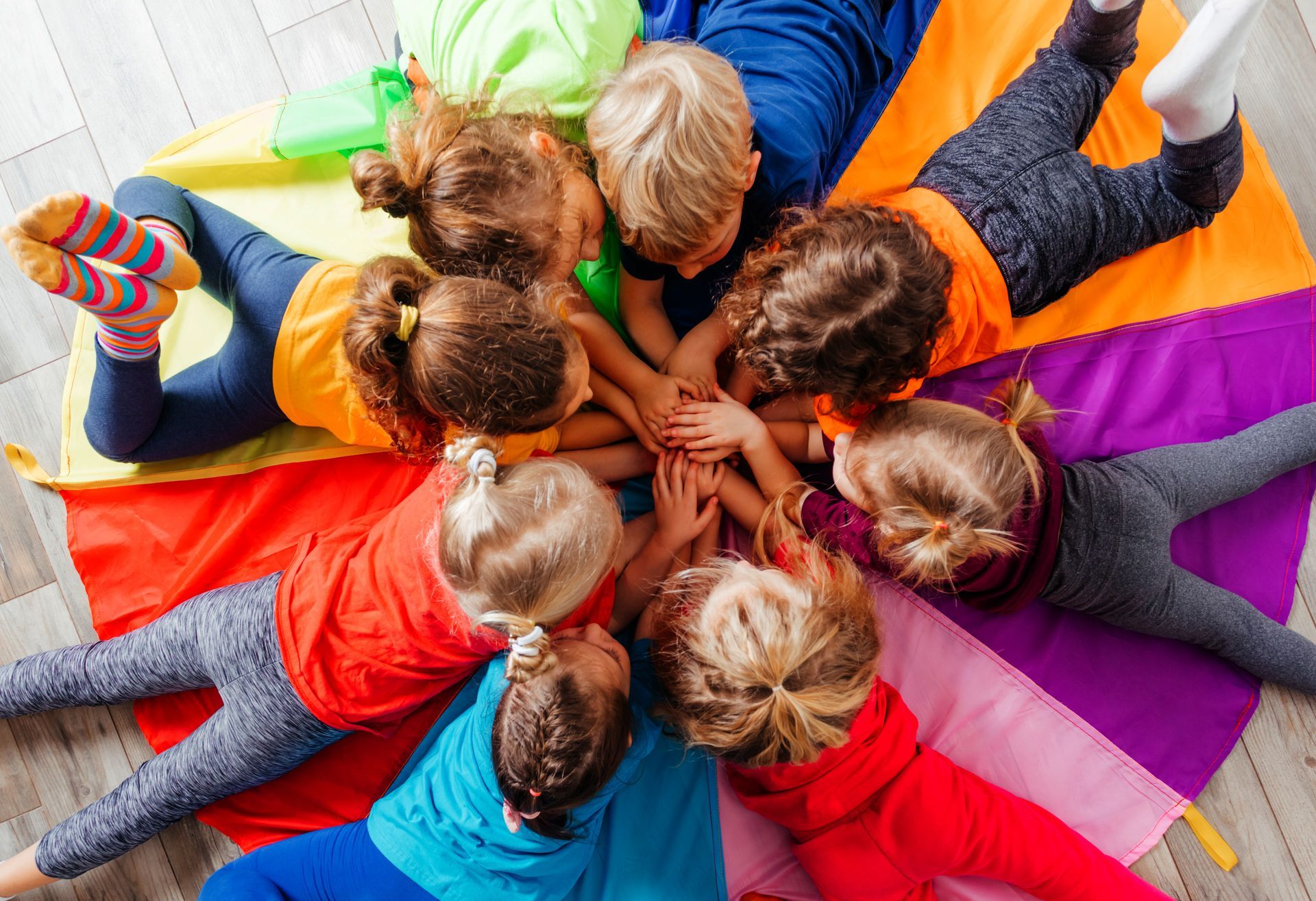 A group of children are laying in a circle on a colorful parachute.