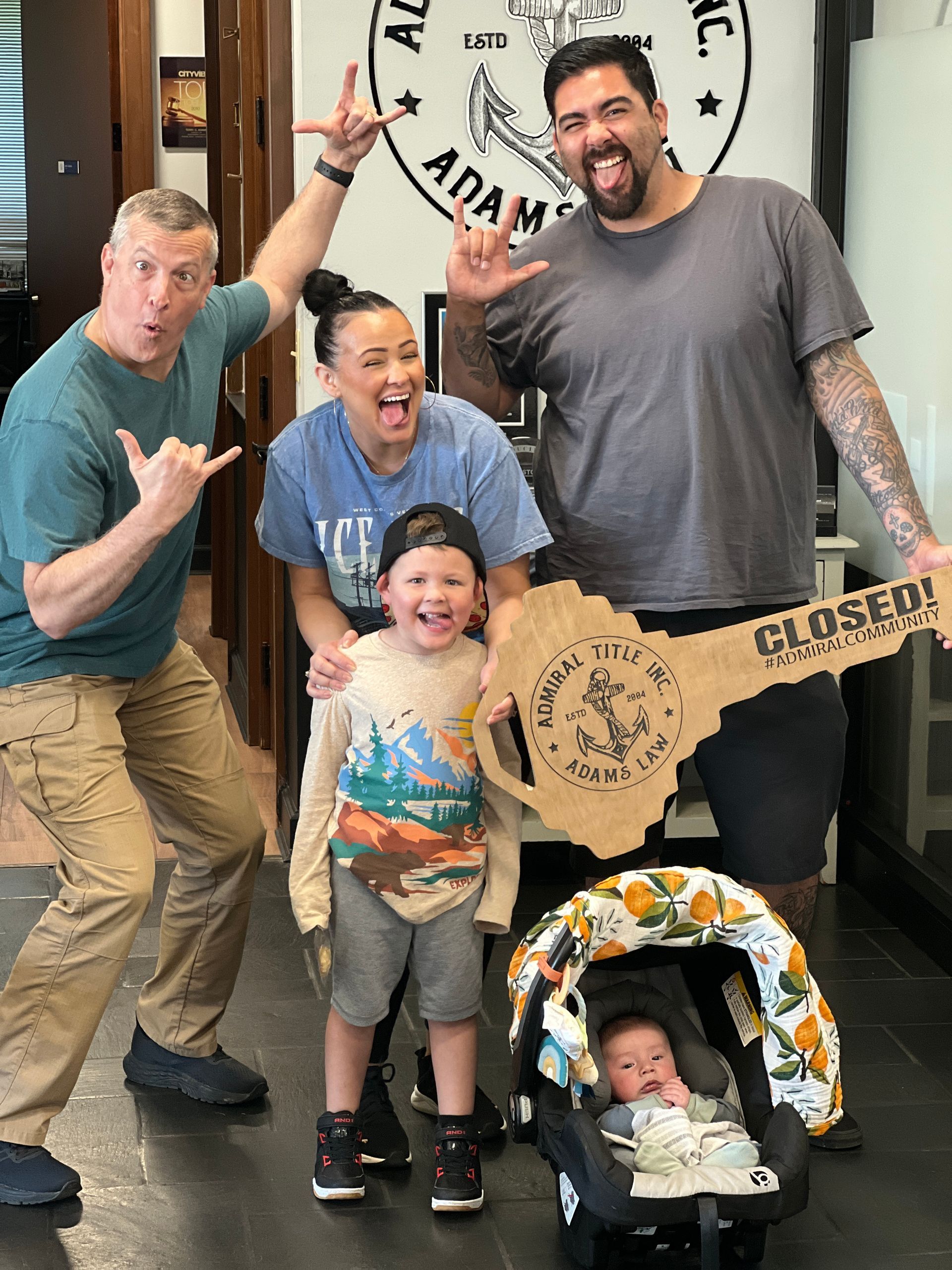 Group posing indoors with a giant cardboard guitar and a baby in a stroller, smiling and making playful gestures.