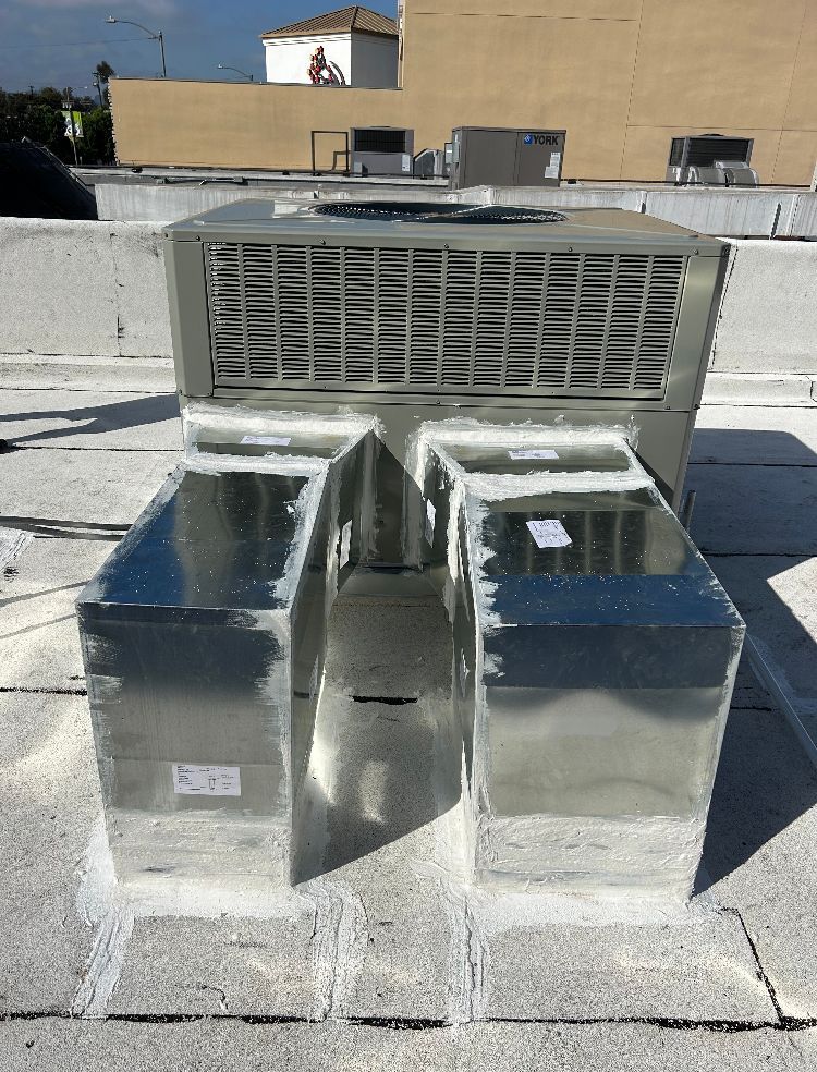 A rooftop HVAC unit with two silver duct boxes, set against a bright, sunny sky.