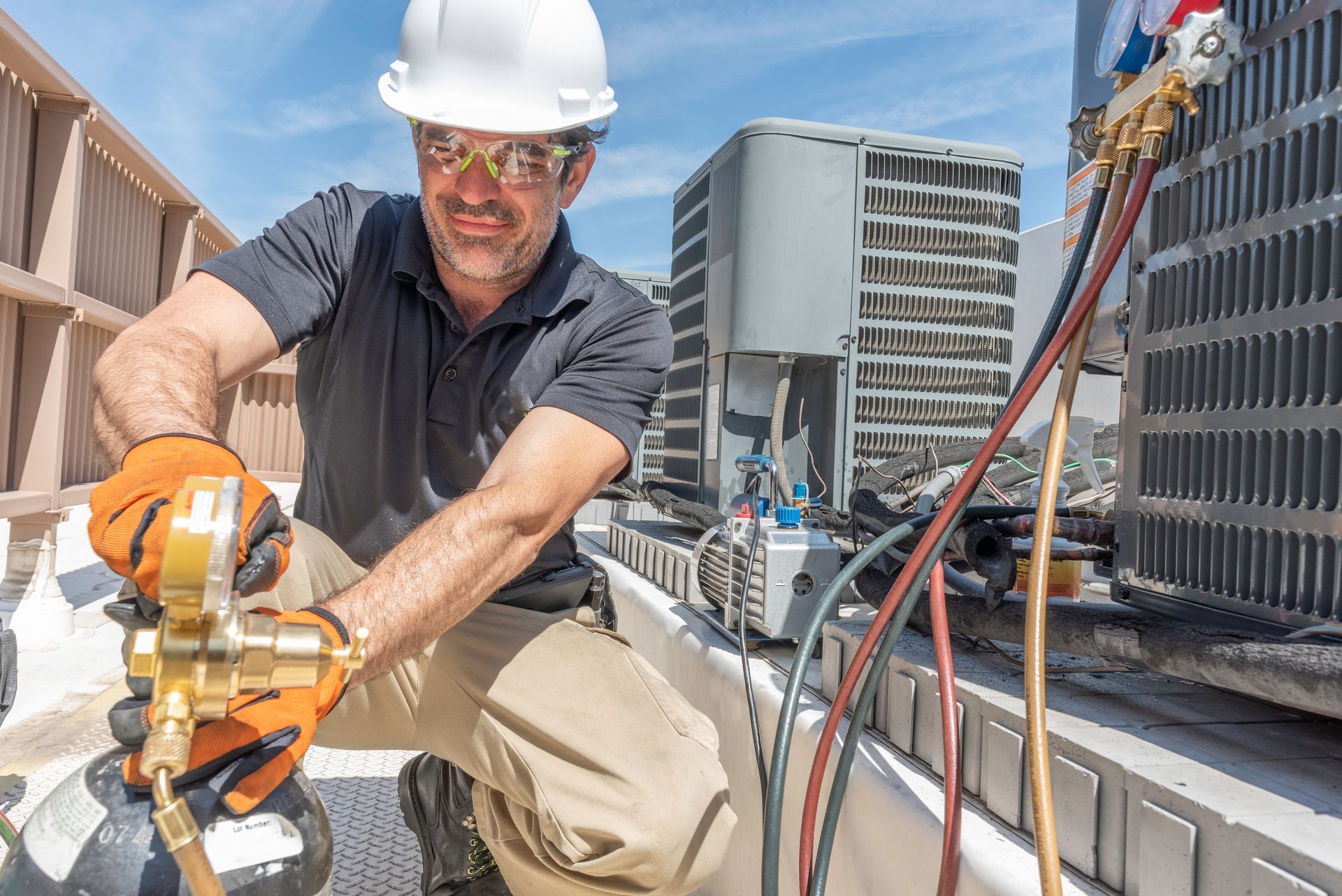 HVAC technician works on air conditioning unit, wearing safety gear outdoors on a sunny day.
