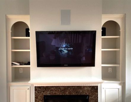Wall-mounted TV above a white fireplace with built-in shelves and cabinets on both sides