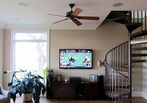 Living room with spiral staircase, ceiling fan, TV, and large window beside a potted plant.