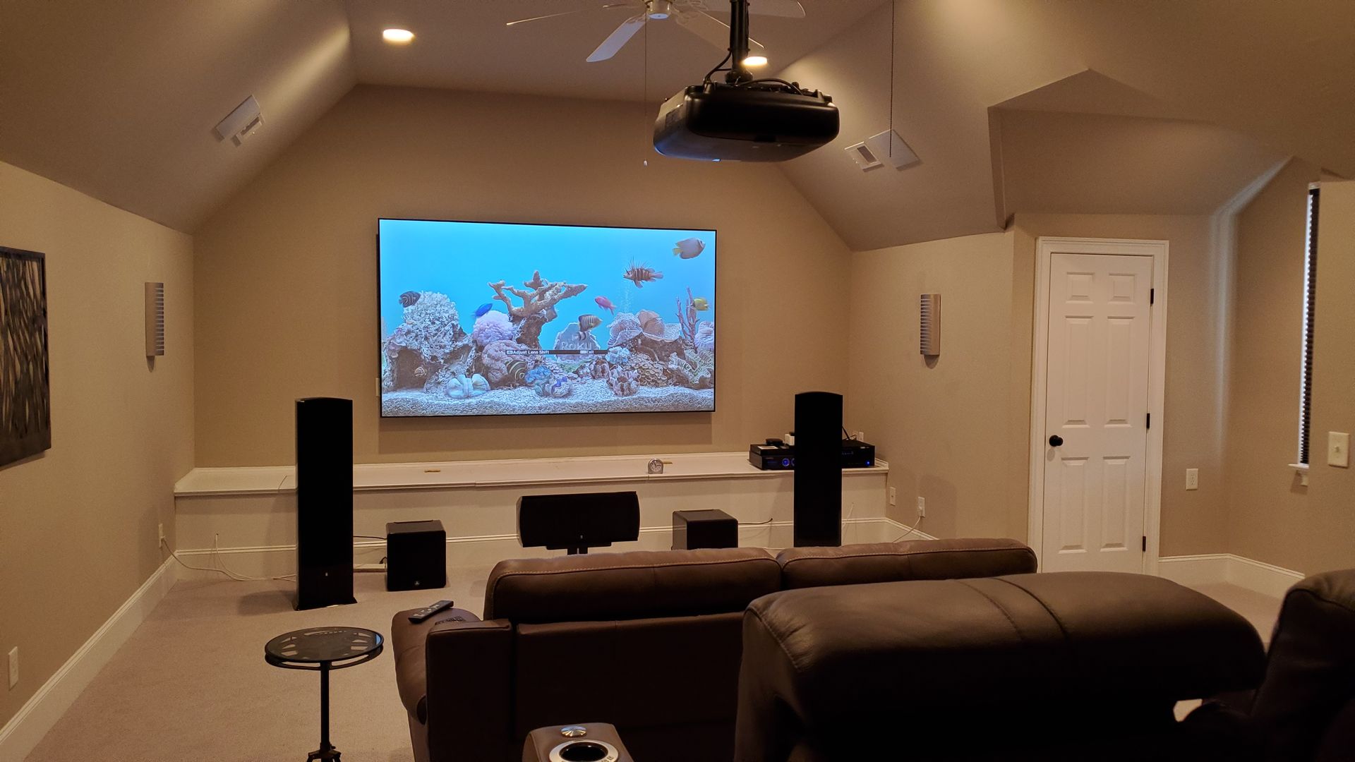 Home theater room with a large wall-mounted screen showing an underwater scene, speakers, and a couch