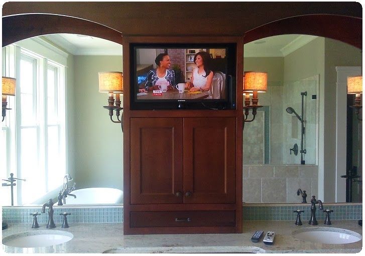 Bathroom vanity with mounted TV between two sinks and mirrors, lit by wall sconces