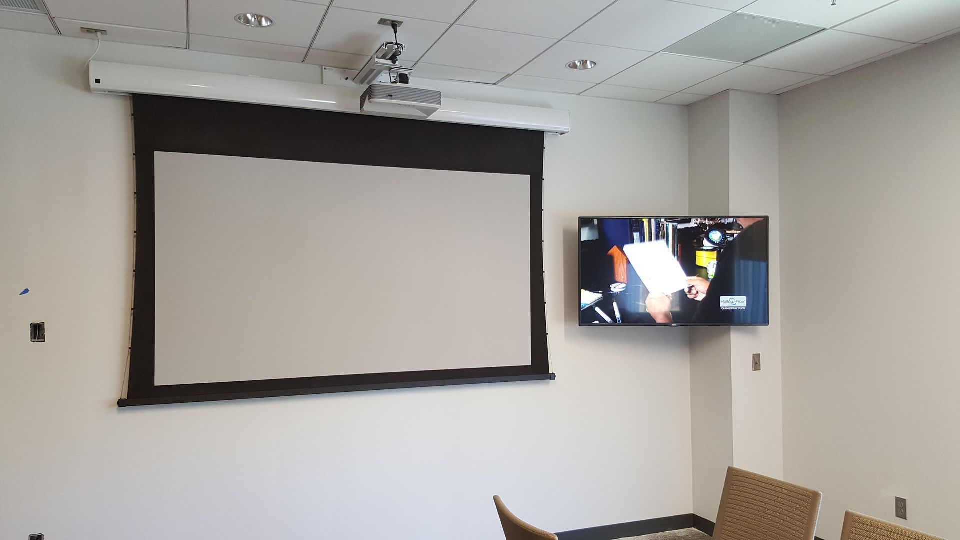 Conference room with a pull-down projector screen and a wall-mounted TV displaying a presentation