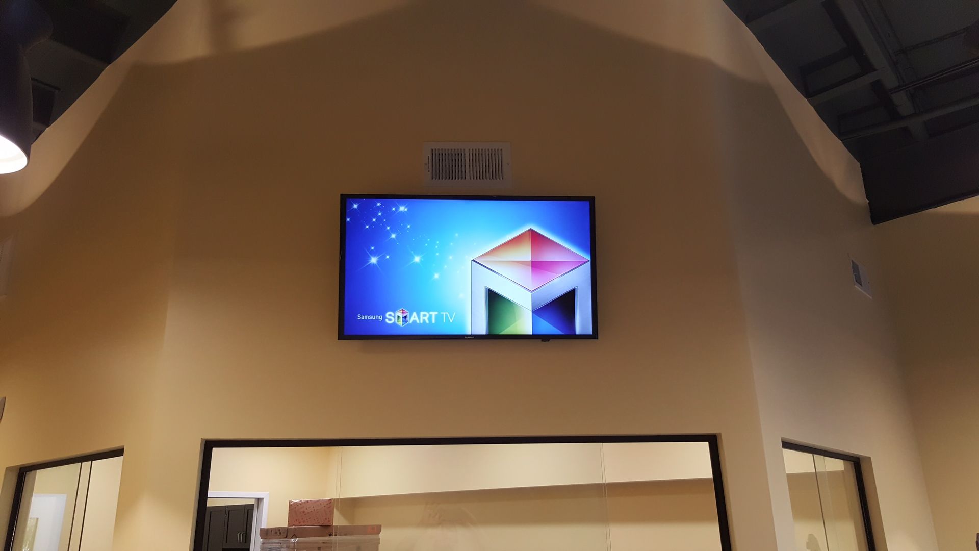 Wall-mounted digital screen above a doorway in a warm-lit interior, displaying a colorful cube graphic.