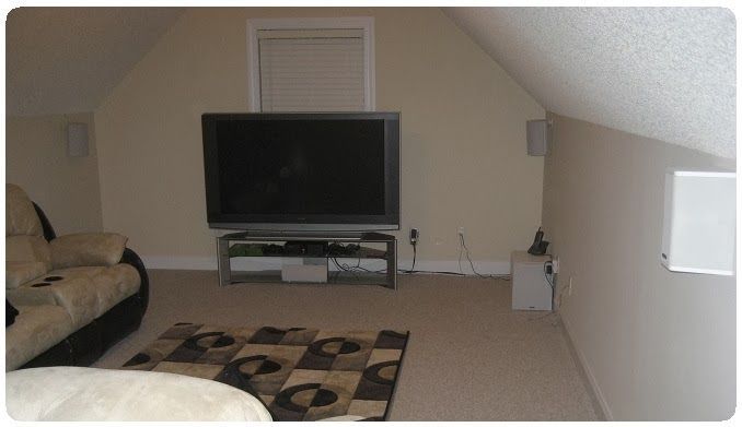 Carpeted attic living room with a TV, sofa, rug, and small table under sloped ceiling
