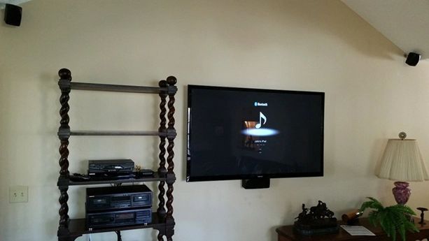 Living room with wall-mounted TV, wooden shelf, stereo system, lamp, and a small plant on a table.
