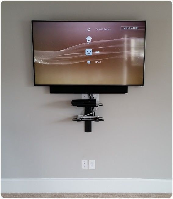 Wall-mounted flat-screen TV above a black bracket on a blank beige wall.