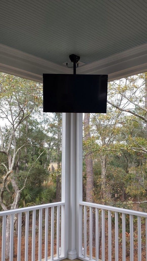 Blank TV mounted on a porch ceiling overlooking trees and a railing.