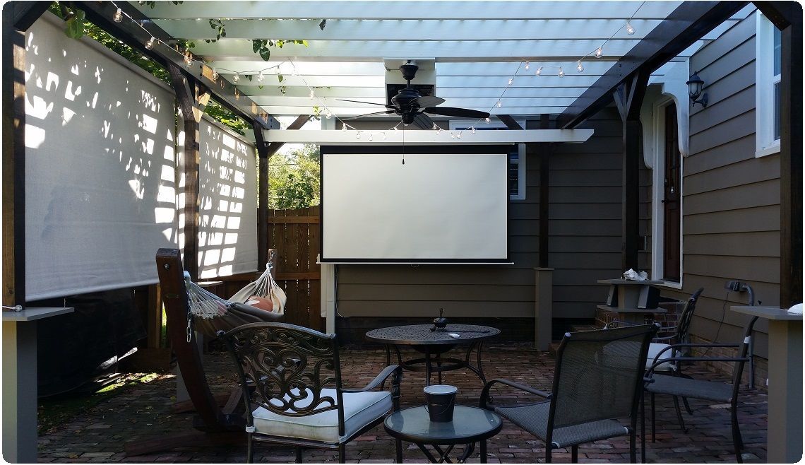 Covered patio with projector screen, wicker chairs, and a glass table in a shaded outdoor seating area