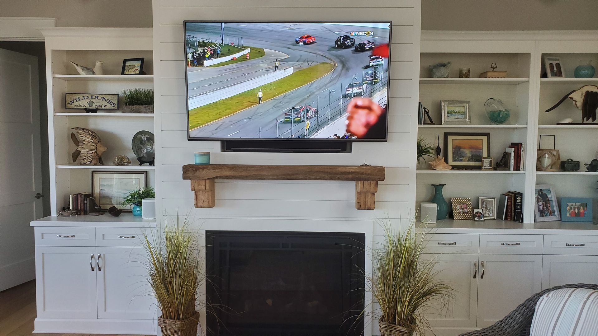 Living room with a wall-mounted TV showing a car race above a fireplace and built-in shelves