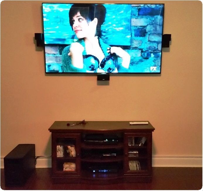 Wall-mounted TV playing a woman’s portrait above a wooden entertainment console in a beige living room