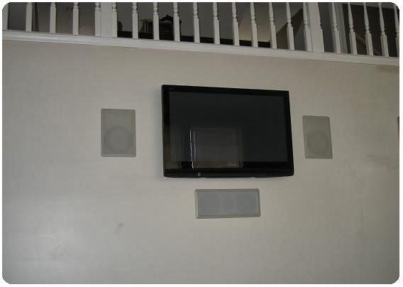 Wall-mounted TV centered on a white wall with two speakers and a vent above
