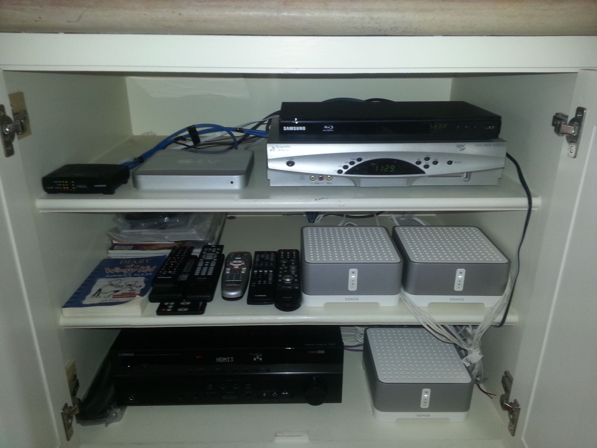 White cabinet shelves with AV equipment, remotes, and gray storage boxes